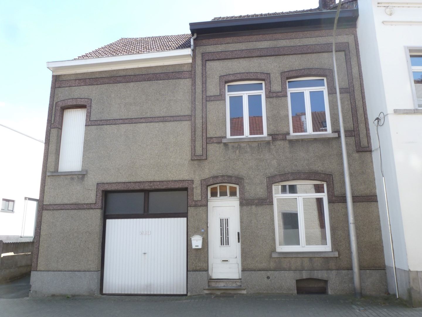 Rijwoning met grijze gevel, witte garagepoort, witte voordeur en witte ramen op twee verdiepingen