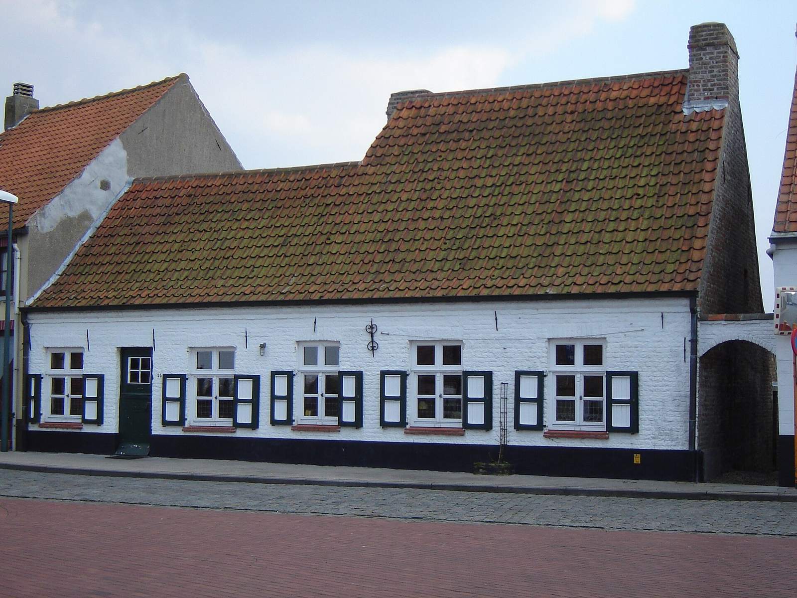 Witgekalkte Vlaamse dorpswoning met rode pannen en een rij ramen met donkere luiken langs de straat